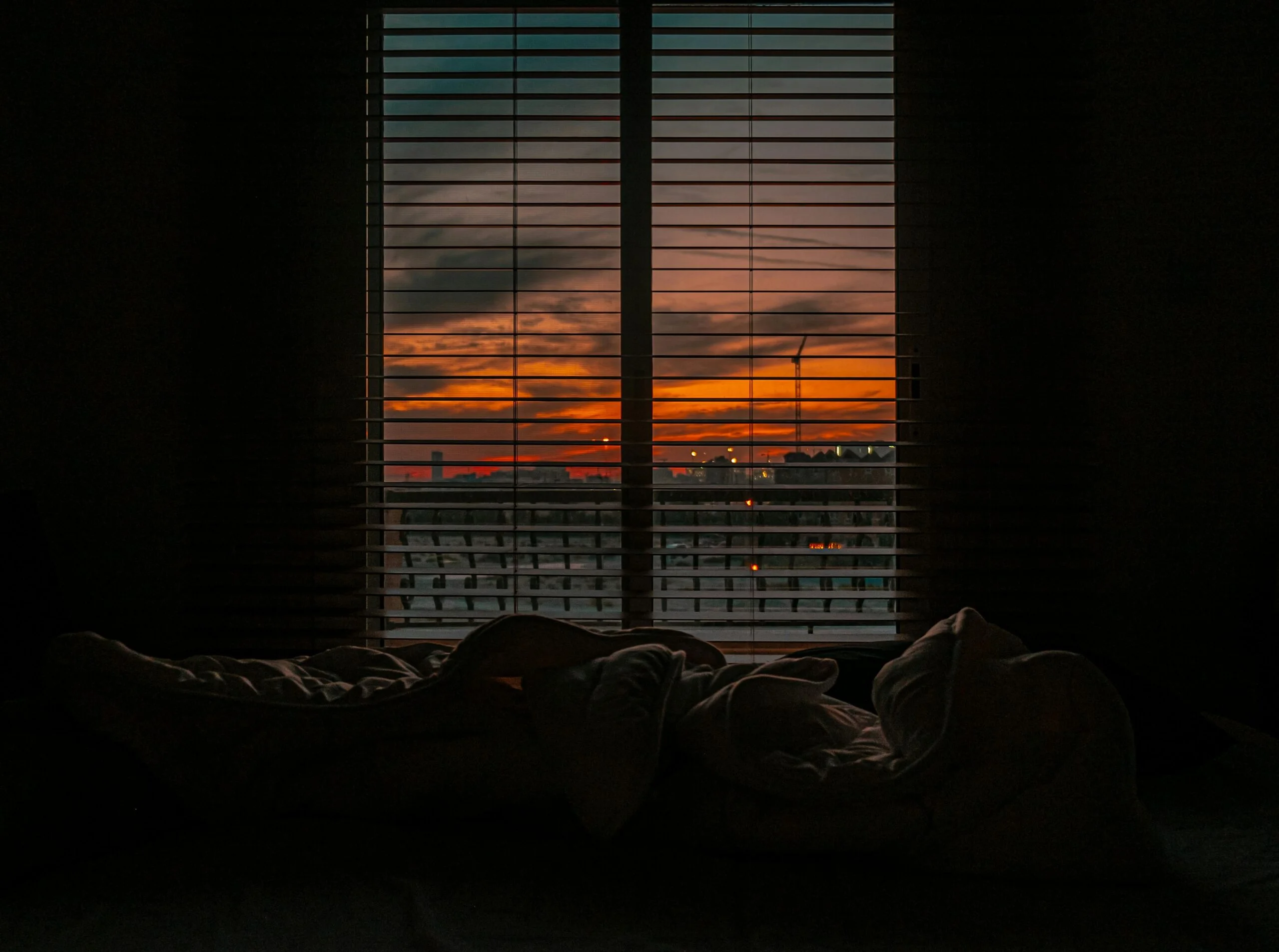 Cozy bedroom with a view of a vibrant sunset through window blinds