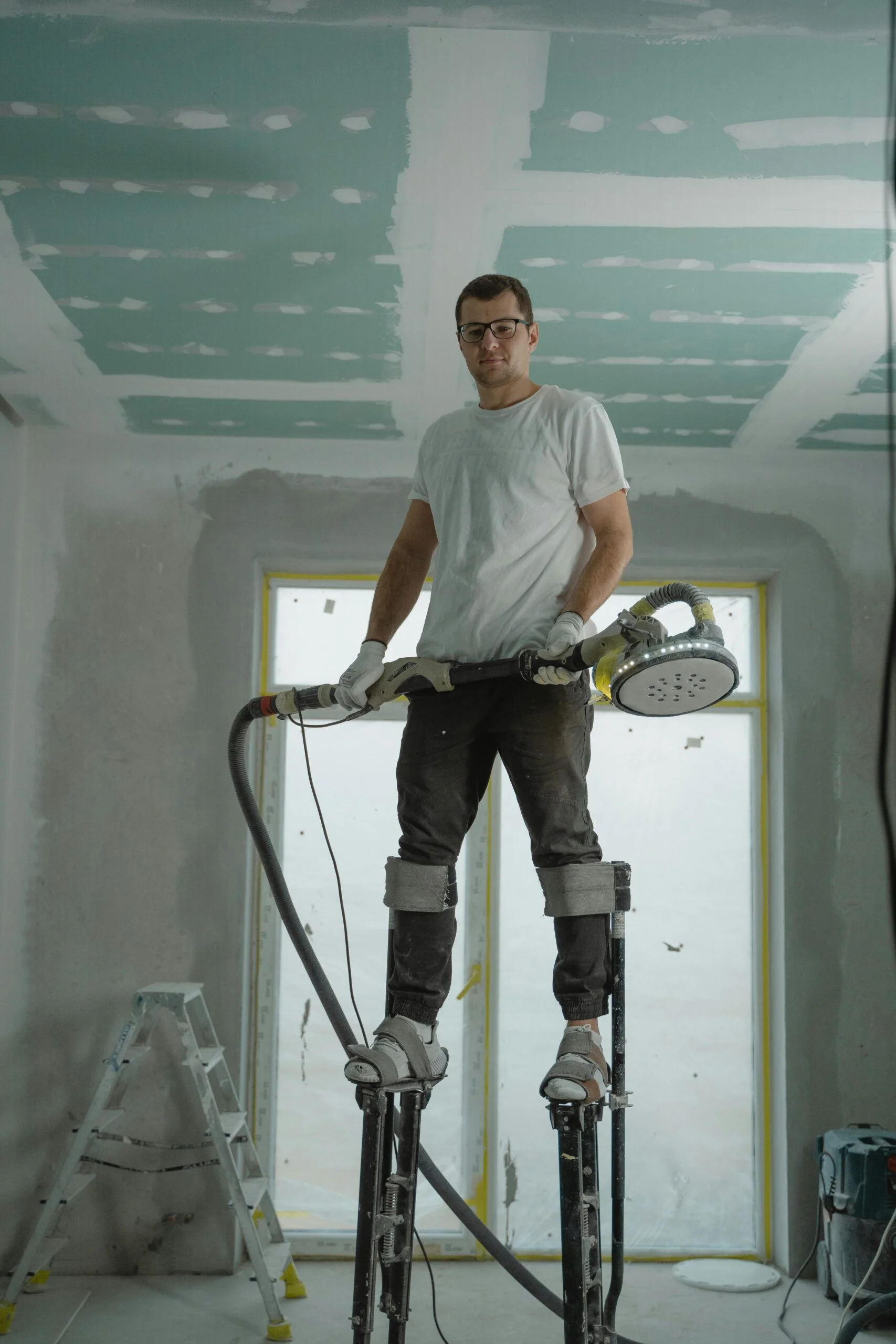 A construction worker using stilts for ceiling renovation indoors