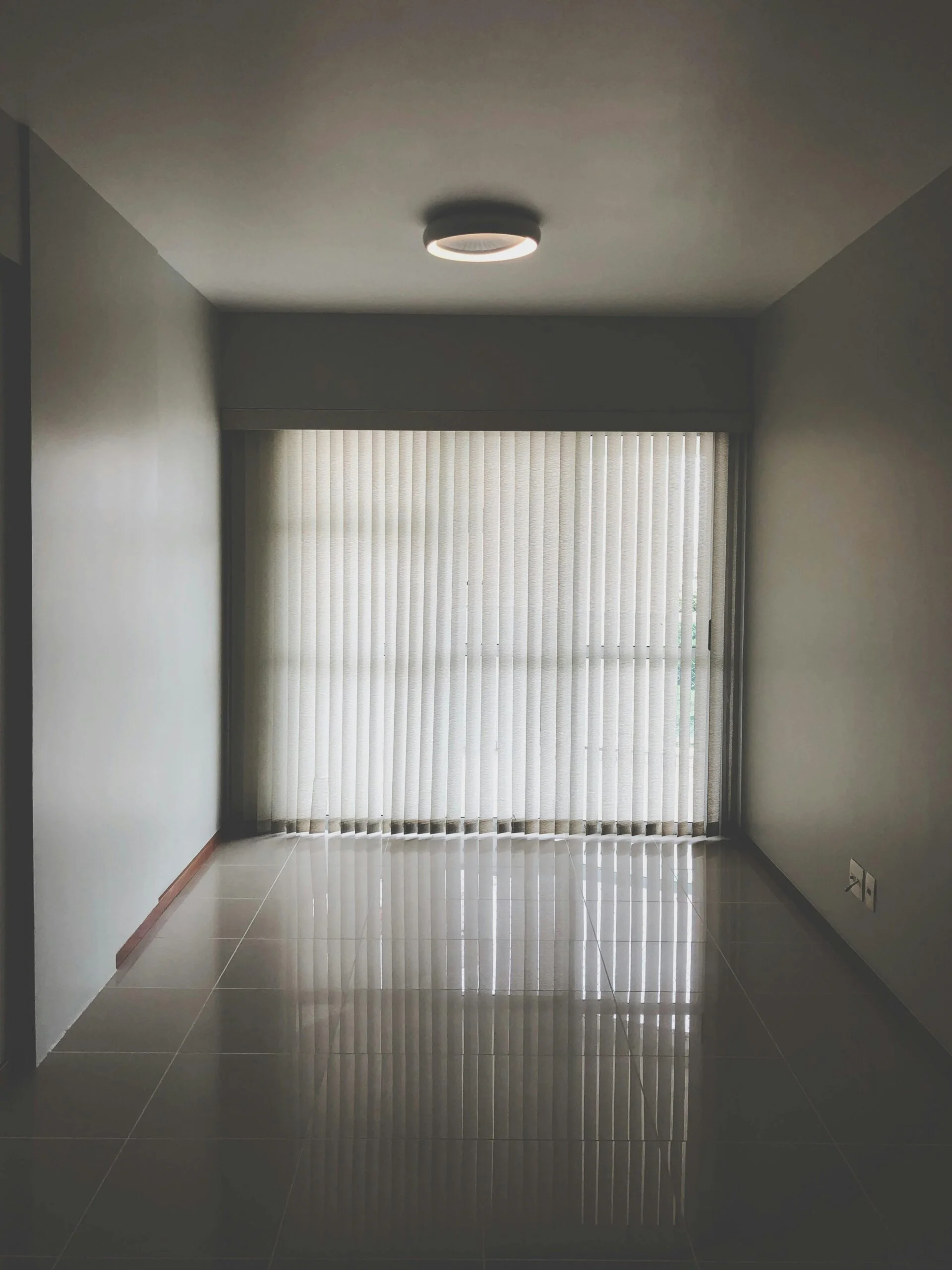 Spacious empty room with modern design featuring large window blinds and tiled floor