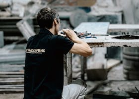 Worker kneeling in an industrial workshop, surrounded by tools and materials.