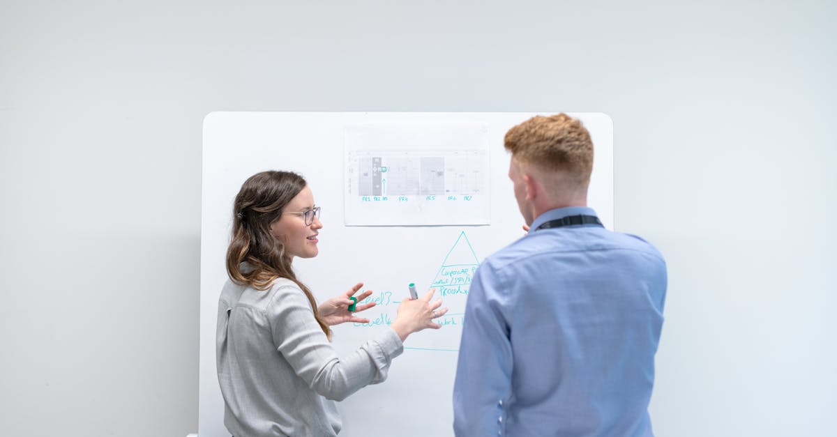 Two professionals discussing project plans at whiteboard in office setting.